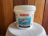 A white plastic bucket labeled 'Crystal Water Calcium Hardener' is placed on a white surface with a wooden background.